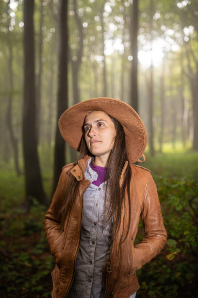 Portrait of mature woman with hat walking in spring forest alone. Peaceful tourism in the woods.
