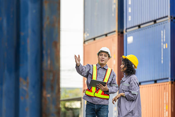 istock Female supervisor in safety gear and foreman worker in hardhat checking and control loading containers box from cargo 2202417465