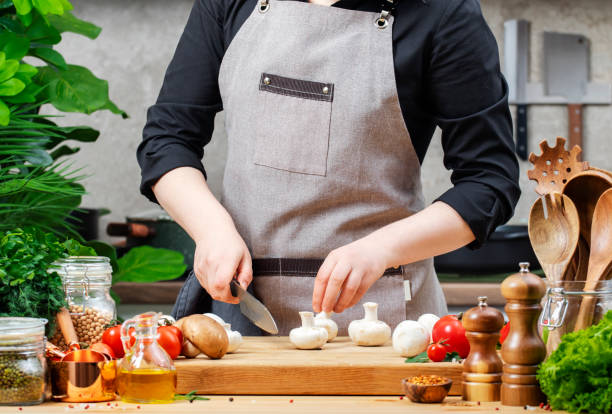 istock Chef holds fresh white champignons and knife in hands/ Cozy kitchen with wooden table, kitchenware, vegetables, herbs and ingredients for cooking. Healthy vegan food, culinary, recipes, food blogging 2202418314