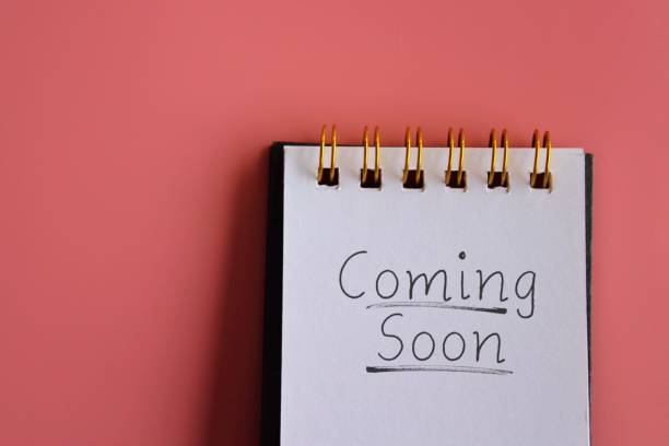 A notepad with the handwritten phrase Coming Soon on a bright pink background. Copy space for text. Announcement, reveal, teaser concept.
