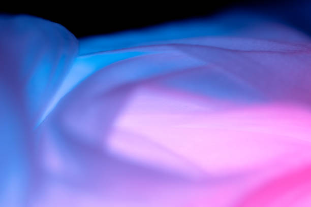 Soft fabric in shades of blue and purple flows gently, illuminated by ambient light, creating a captivating and dreamy visual effect. The interplay of colors enhances the elegant texture.