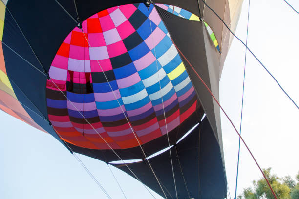 Middle aged man inflating hot air balloon outdoors, holding fabric and preparing equipment, close up of hands and torso with colorful balloon in background