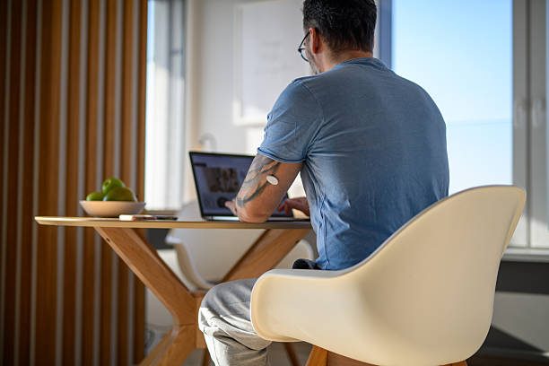 istock Man with CGM sensor on arm sitting at table and working on laptop. 2202431383