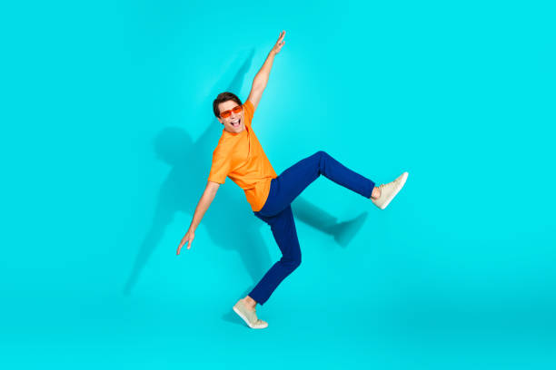 istock Young man posing dynamically on bright turquoise background wearing casual orange shirt and blue pants 2202436165