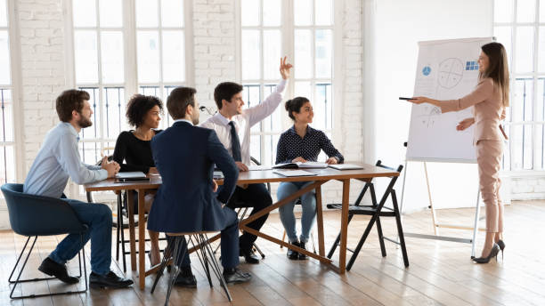 istock Group meeting participant raising hand to ask trainer question 2202440068