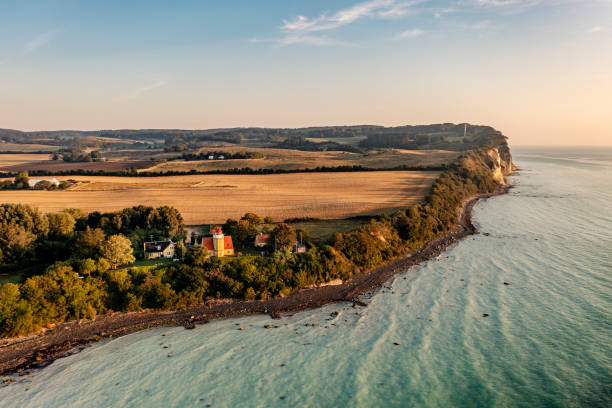Drone view of the island of Moen in Denmark. Moens Fyr or Lighthouse can be seen in the bottom half of the picture, looking out over the Baltic Sea. In the background, the cliffs at Moens Klint can be seen. They rise to 100m high and run for 11 km along the Baltic Sea coastline—colour, vertical with some copy space. The green and turquoise colors in the water are due to the amount of chalk. Landslides from the nearby chalk cliffs wash thousands of tonnes of chalk into the water, with sea currents spreading this around the coastline—colour, horizontal with some copy space.