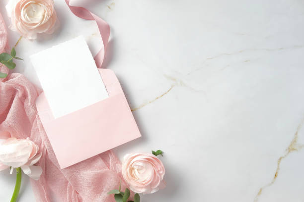 istock Pink envelope with blank card, surrounded by pink flowers and fabric on a marble background. Perfect for wedding invitations, greeting cards, or romantic messages 2202443199
