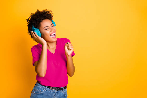 istock Copyspace photo of curly wavy cheerful charming lady singing into her imaginary microphone wearing jeans denim wireless earphones isolated over yellow vibrant color background 2202444883