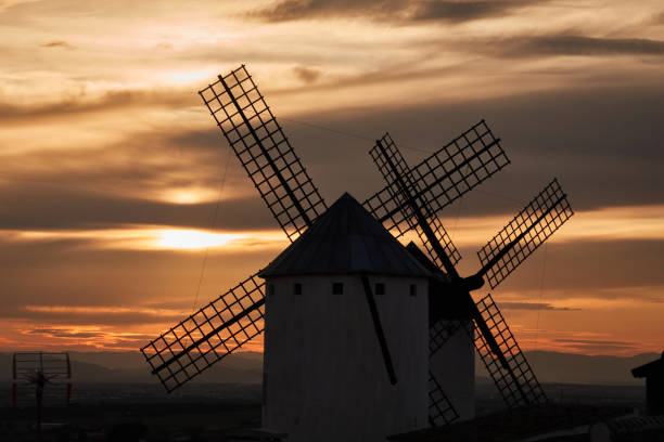 Sunset over the windmills of Campo de Criptana, casting a golden glow on the iconic landscape of Castilla-La Mancha, Spain, famously linked to Don Quixote