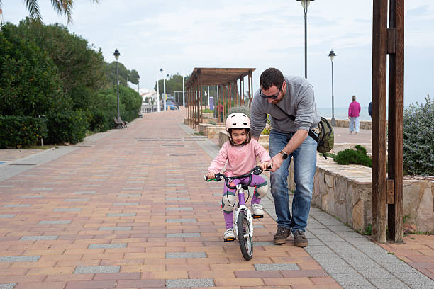 Father teaching his 4 year old daughter to pedal a bicycle.