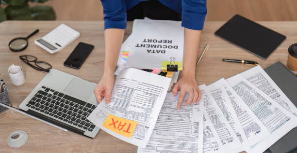 istock Accountant sorting tax paperwork and using a laptop in a contemporary office setting. 2202449430