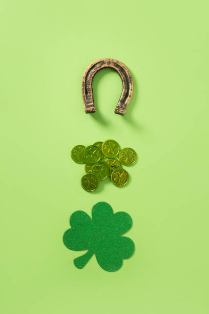 St. Patrick's day creative minimal composition with clover leaf, green coins and horseshoe on light green background. View from above.