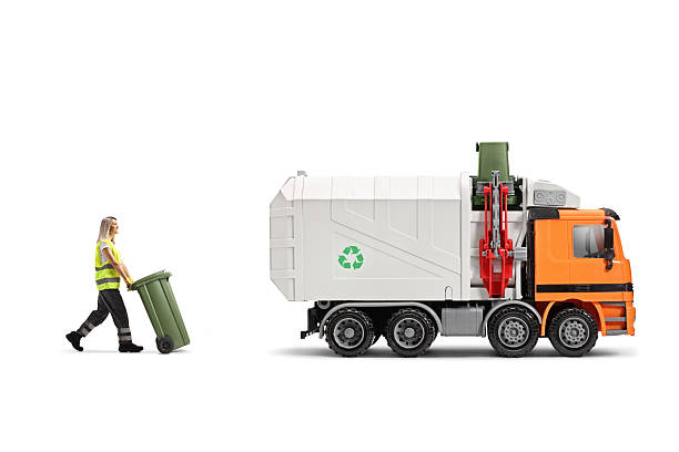 Female waste collector pulliung a bin and walking towards a garbage truck isolated on white background