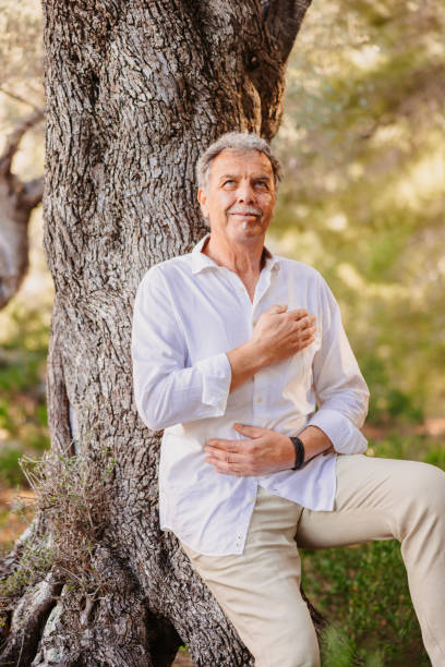 istock 65-year-old gray-haired mature man sitting peacefully against an ancient olive tree with his eyes closed and a smile as he embraces the moment of mindfulness 2202453436