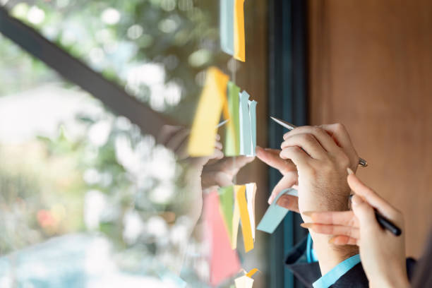 istock Collaborative business team brainstorming ideas with sticky notes on a glass wall in a modern office. 2202454218