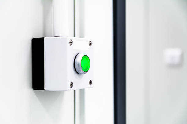 istock Green illuminated emergency stop button on white industrial wall 2202455284