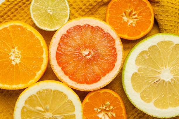 A close up of several oranges and a grapefruit. The oranges are all different colors, including yellow, orange, and green. The grapefruit is also orange, but it is larger than the other fruits