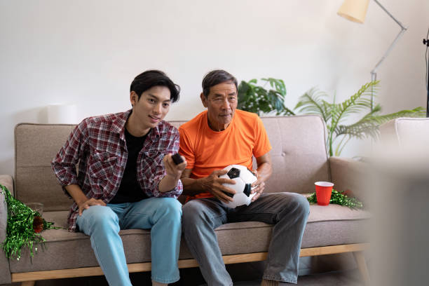 istock Multicultural family watching a soccer match at home, sharing joy and camaraderie while holding a soccer ball. 2202457202