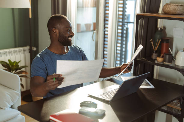 istock Smiling man working from home using laptop and documents in living space 2202457870