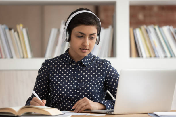 istock Indian female student in headphones make notes studying online 2202468441