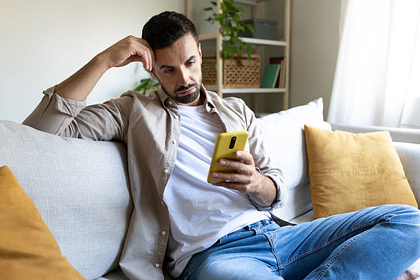 istock Pensive man reading smartphone messages while relaxing on sofa at home 2202469301