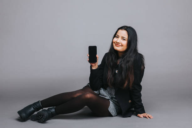 istock Indian woman presenting smartphone on grey background 2202469586