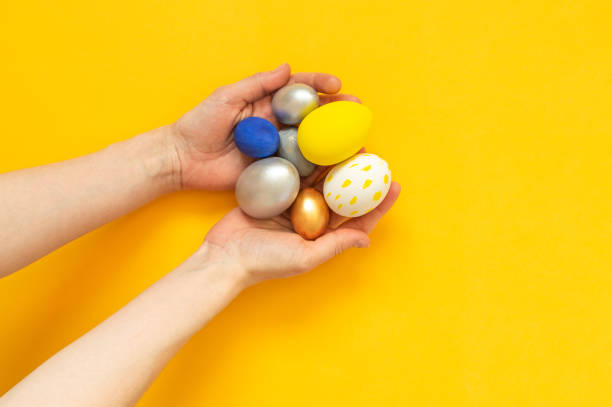 istock Women's hands holding colored decorated eggs on a yellow background.Happy Easter 2202471097