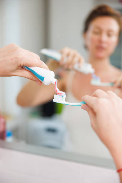 istock Woman squeezing toothpaste on toothbrush in front of the bathroom mirror 2202472427
