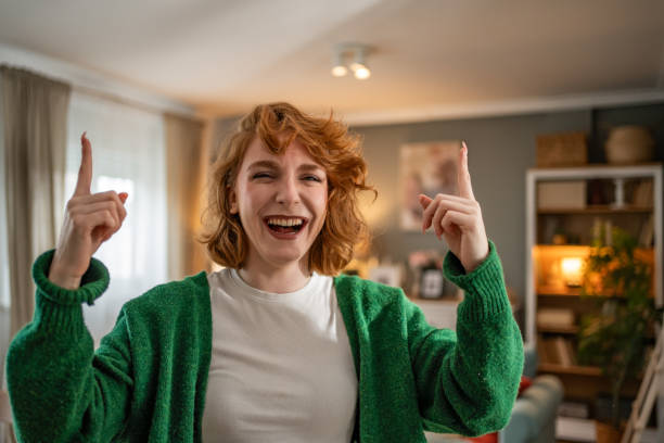 istock Young woman pointing upwards and laughing at home 2202472621
