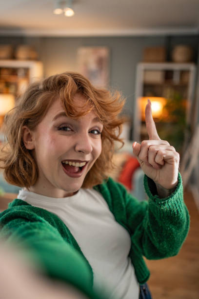 istock Young woman taking a selfie and pointing up with excitement 2202472737