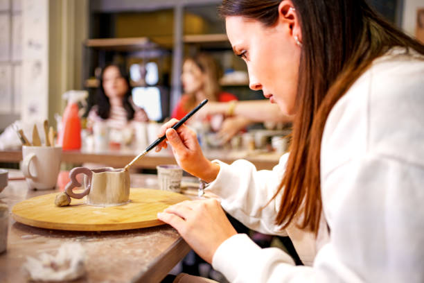 A young woman carefully paints a small clay cup during a pottery class