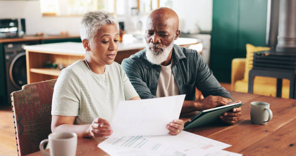 istock Mature, interracial couple and documents with tablet for financial discussion, planning or expenses at home. Man, woman or mortgage with paperwork or technology for payment due, finance or bills 2202474484