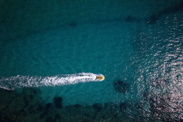 La Spezia, Italy - July 20, 2022: Small black and orange motorized dinghy with a family on board (a man, a woman and a boy), on a sunny summer day in the blue Mediterranean sea, Tellaro, Lerici municipality, Gulf of La Spezia or Gulf of Poets, Liguria, Italy, southern Europe.