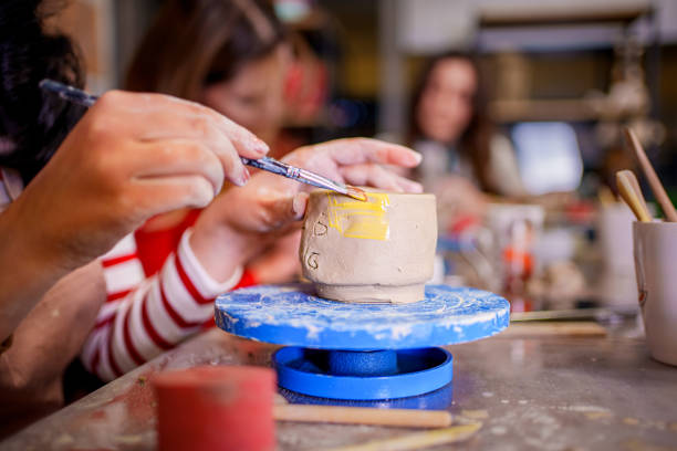 A young woman carefully paints a small clay cup during a pottery class