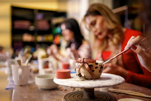 A young woman carefully paints a small clay cup during a pottery class