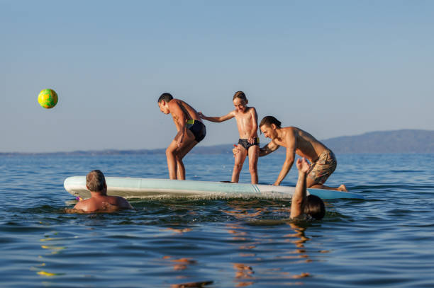 Family joy unfolding on the calm sea as a father and his children engaging in a playful balancing game on a floating surfboard