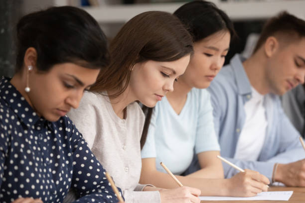 istock Concentrated multiethnic students busy writing test in classroom 2202481498