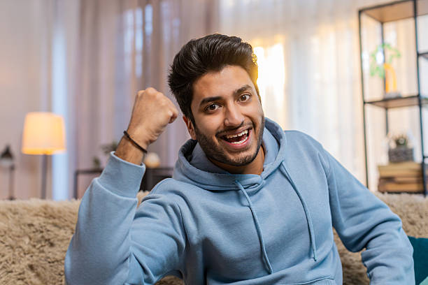 istock Happy Indian young man celebrating success and victory shouting while sitting on sofa at home 2202488409