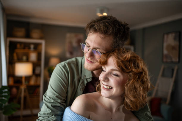 A young couple hugging and laughing together in a modern apartment, sharing a cozy moment filled with love and connection, radiating warmth and joy in their intimate space