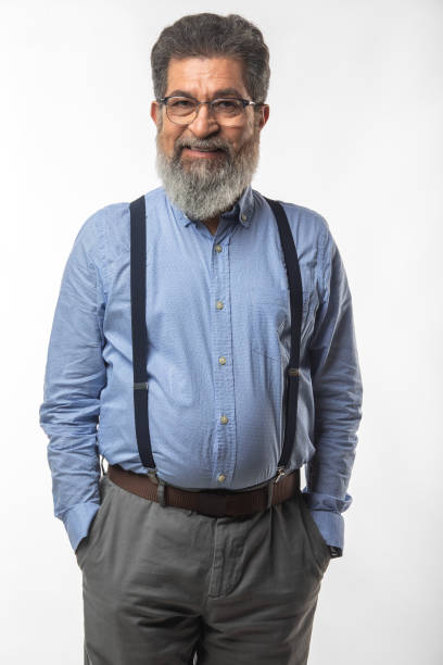 Portrait of bearded senior businessman dressed in suspenders smiling and posing against white background