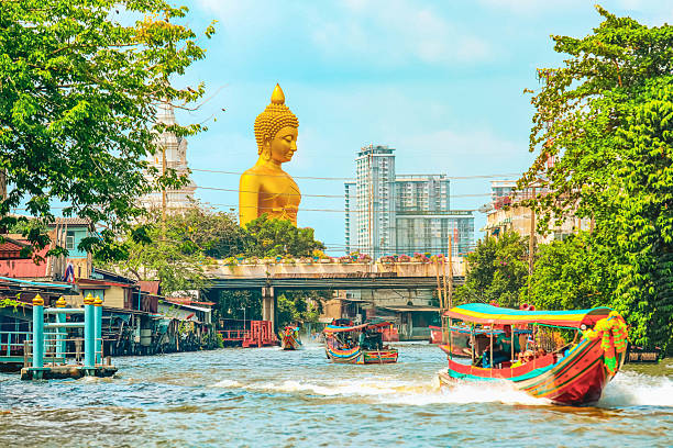 View of big  Buddha statue in Bangkok, Thailand (Wat Pak Nam Phasi Charoen) from canal with wooden houses and long tails boats
