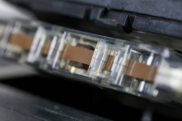 A close-up view of a compact cassette inserted into a tape recorder. A fragment of the tape is visible in the front of the cassette.