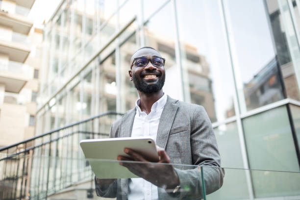 istock Confident businessman with tablet standing outside modern office building 2202516837