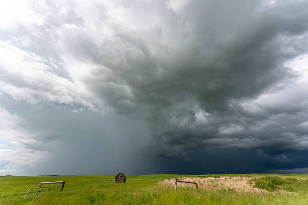 Dramatic supercell storm clouds gathering over a green field with an abandoned house