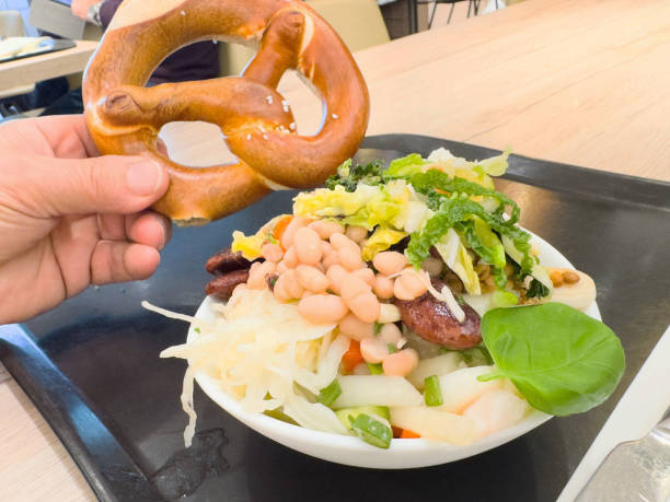 Hand holding pretzel with mixed salad bowl on a tray in a cafeteria setting, restaurant concept