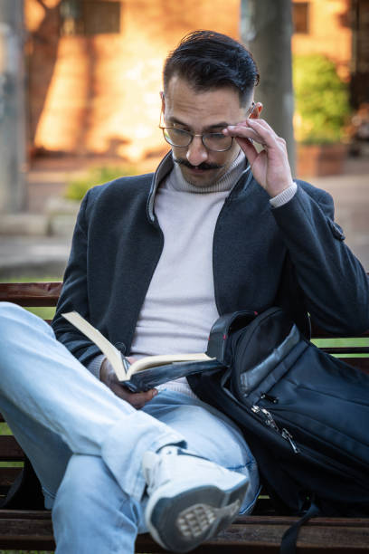 Hispanic man sitting in a park reading a book