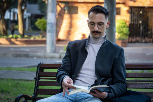 istock Hispanic man sitting in a park reading a book 2202530620