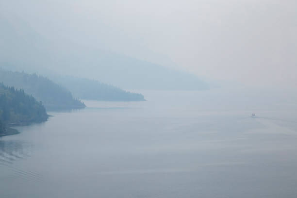 Small boat sailing on a misty lake surrounded by hills, creating a serene and atmospheric scene