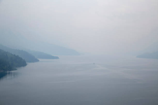 Small boat navigates through the mist on a serene lake, with hills fading into the background