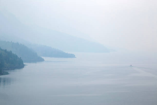 Small boat is sailing on the calm waters of a misty fjord surrounded by mountains